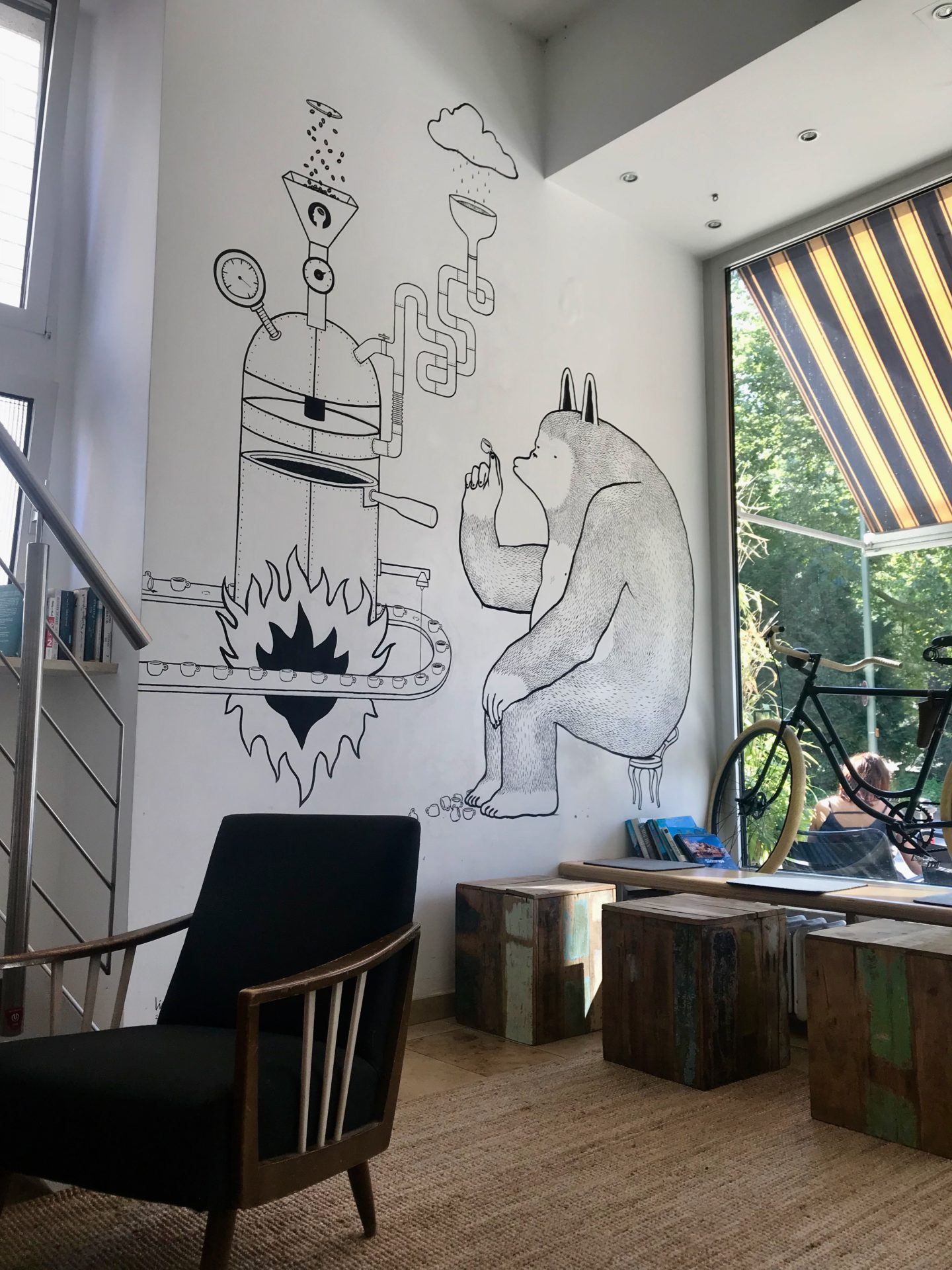 Black and white mural on a coffee shop wall with a big bear-like creature drinking coffee from a tiny cup, and a complicated coffee brewing machine in front of them. Best Coffee Shops in Heidelberg: Coffee Nerd